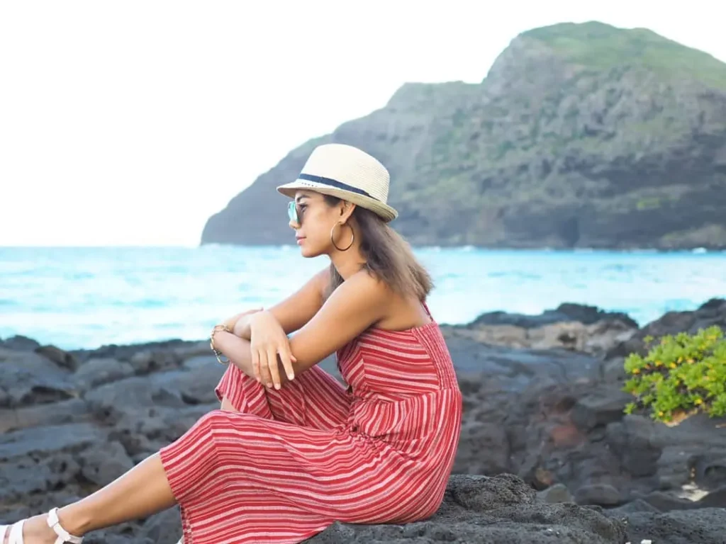 Woman wearing a red striped dress and sun hat on a rocky beach