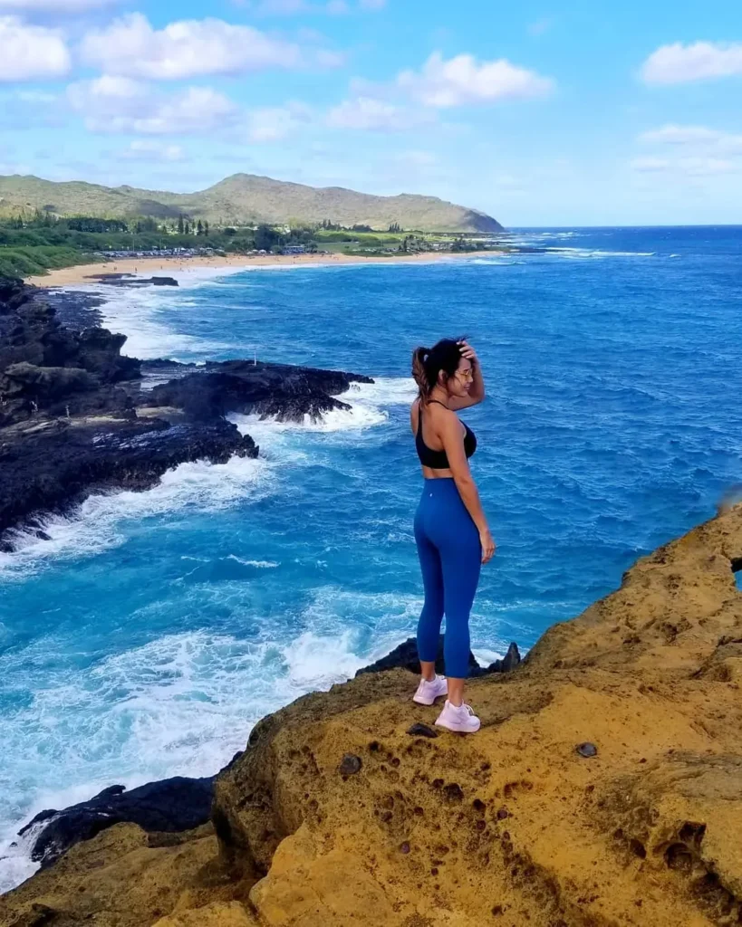 Woman wearing blue leggings, a black top, and sneakers on a coastal hike