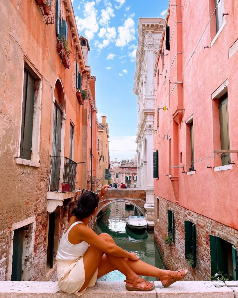 Woman wearing a white tank top, shorts, and sandals while exploring a European canal city