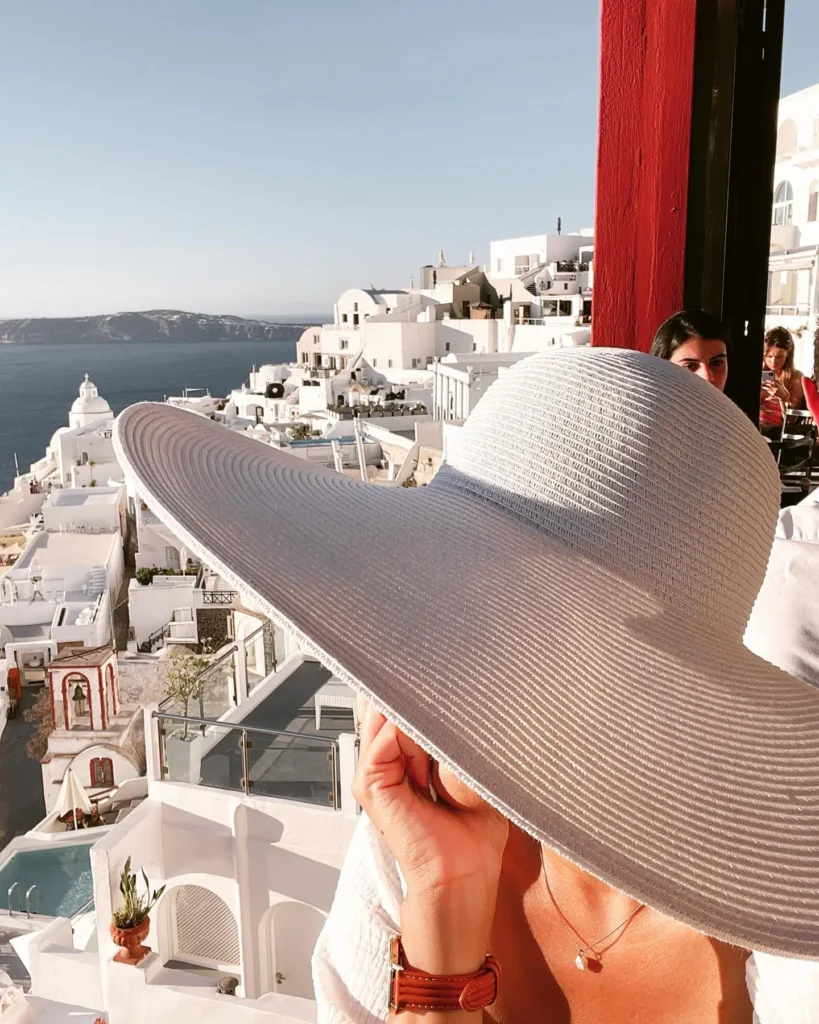 Woman wearing a wide-brim sun hat and white summer outfit overlooking a Mediterranean coastal town