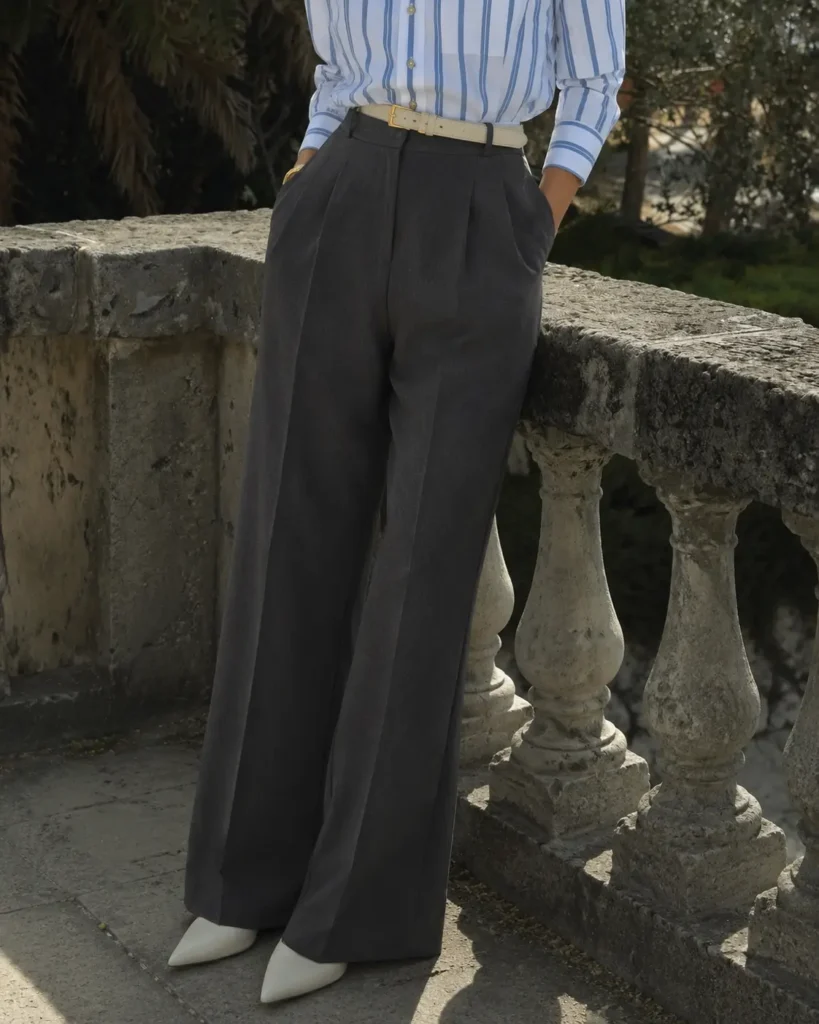 Woman wearing charcoal tailored wool trousers with a blue striped shirt in an old money capsule wardrobe outfit.