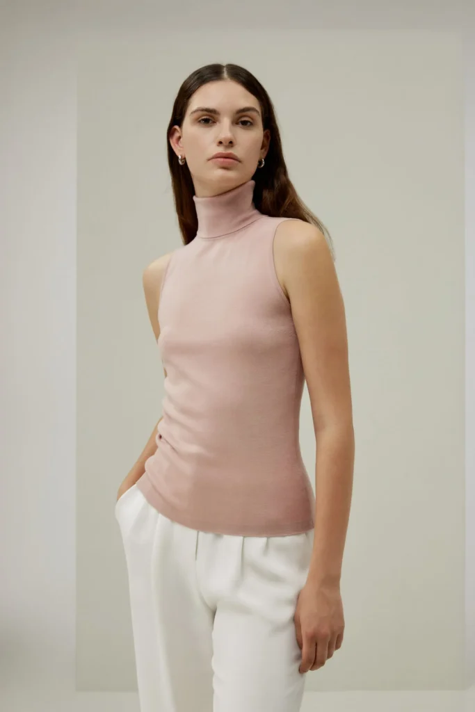 Soft pink sleeveless turtleneck styled with white tailored trousers